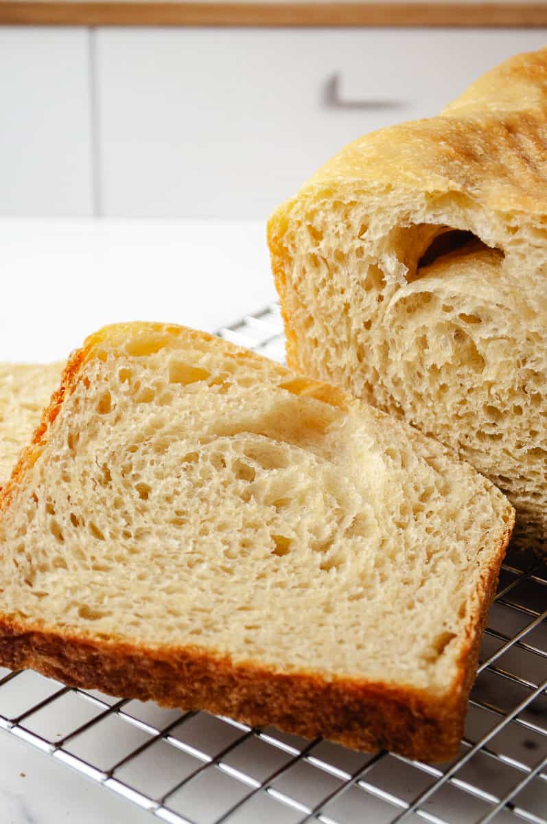 Close-up of freshly sliced sourdough white bread with a soft, open crumb structure and crispy golden crust, resting on a stainless steel cooling rack.