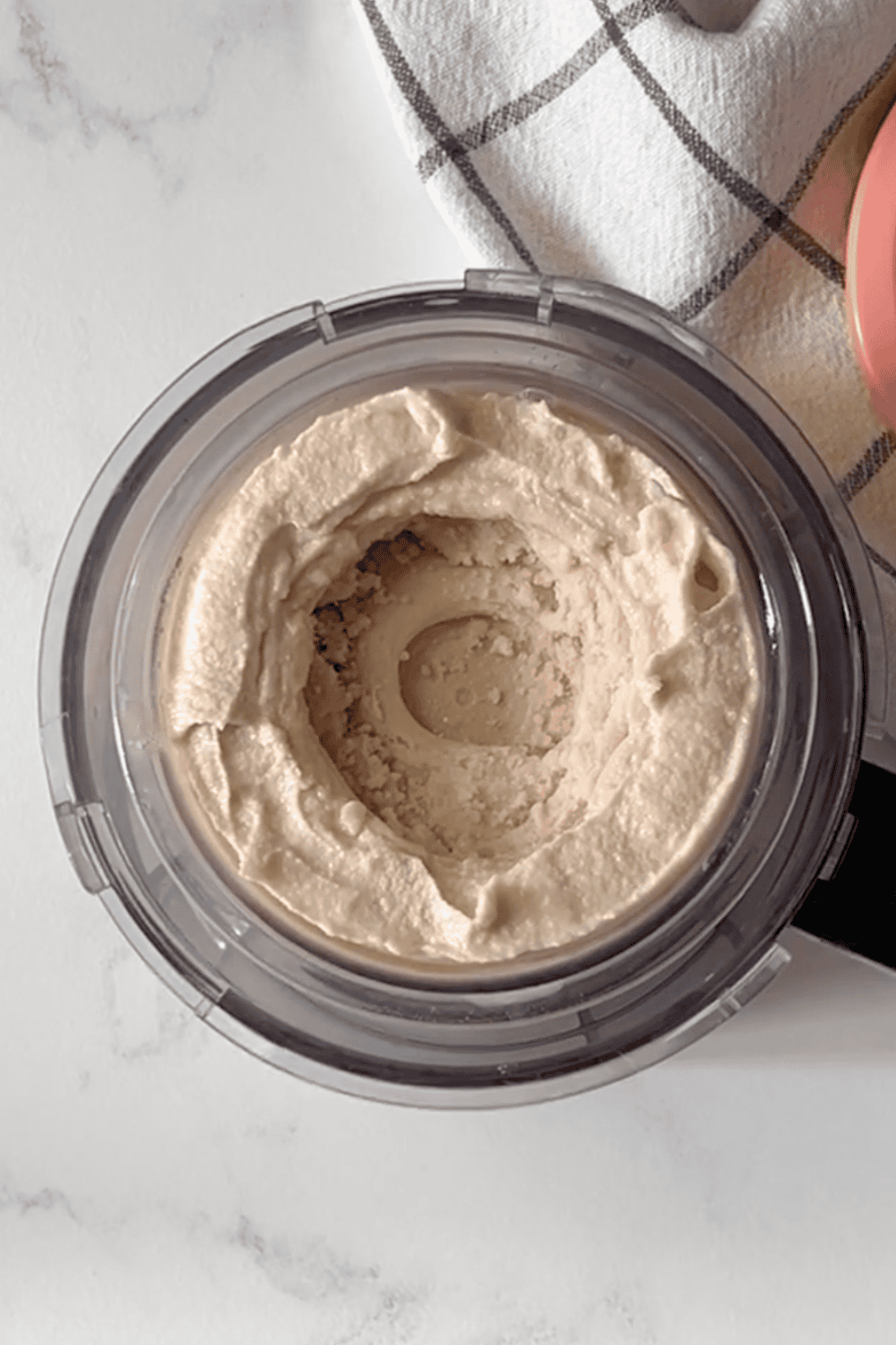 Overhead view of a freshly spun Ninja Creami pint showing smooth and creamy chocolate peanut butter protein ice cream just after spinning, on a white marble surface with a plaid kitchen towel in the background.