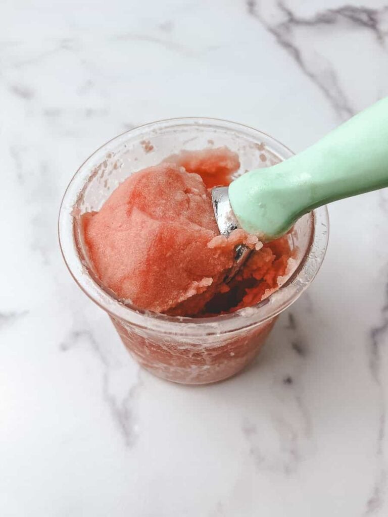 Overhead view of watermelon sorbet in a Ninja Creami pint with an ice cream scoop pulling a scoop from the top