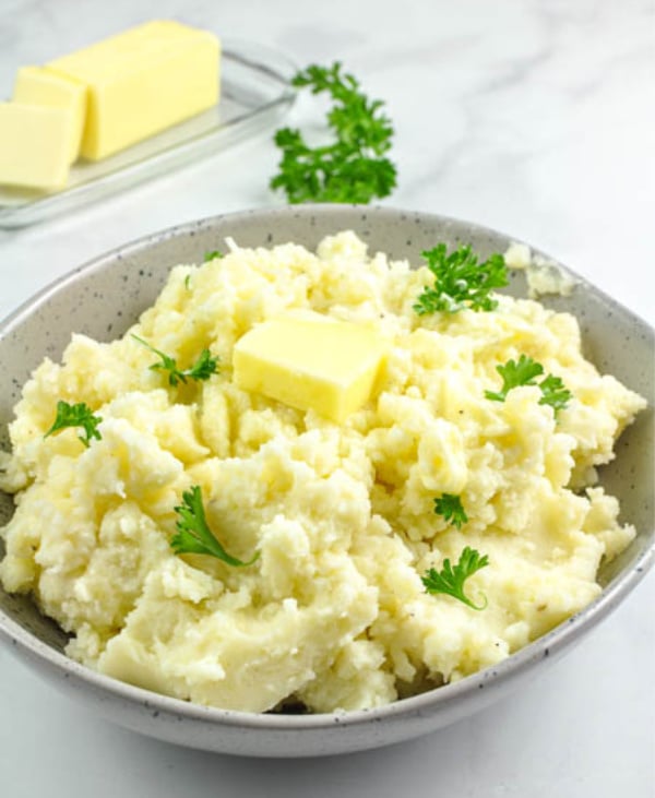 Creamy mashed potatoes recipe made with a potato ricer, served in a speckled bowl with butter and fresh parsley