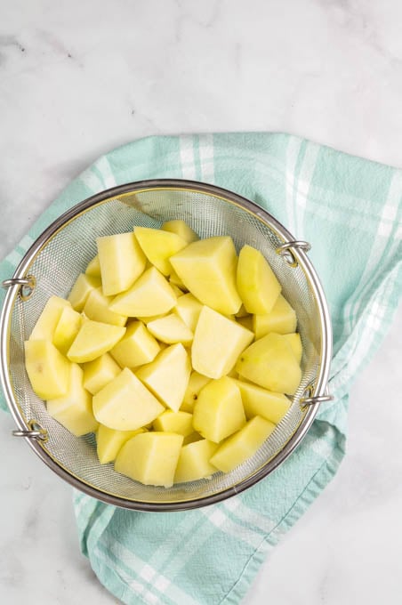 Peeled and cut potatoes in a strainer, ready to boil for homemade mashed potatoes