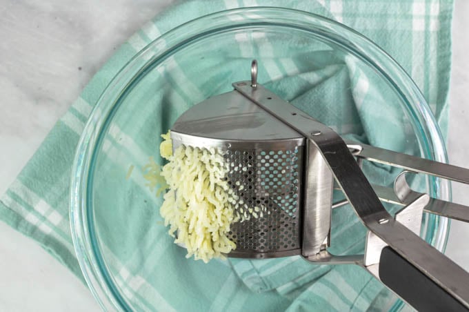 Pressing boiled potatoes through a potato ricer for lump free mashed potatoes