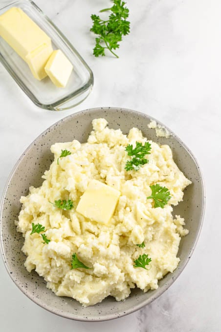 Overhead view of homemade mashed potatoes with butter and fresh parsley