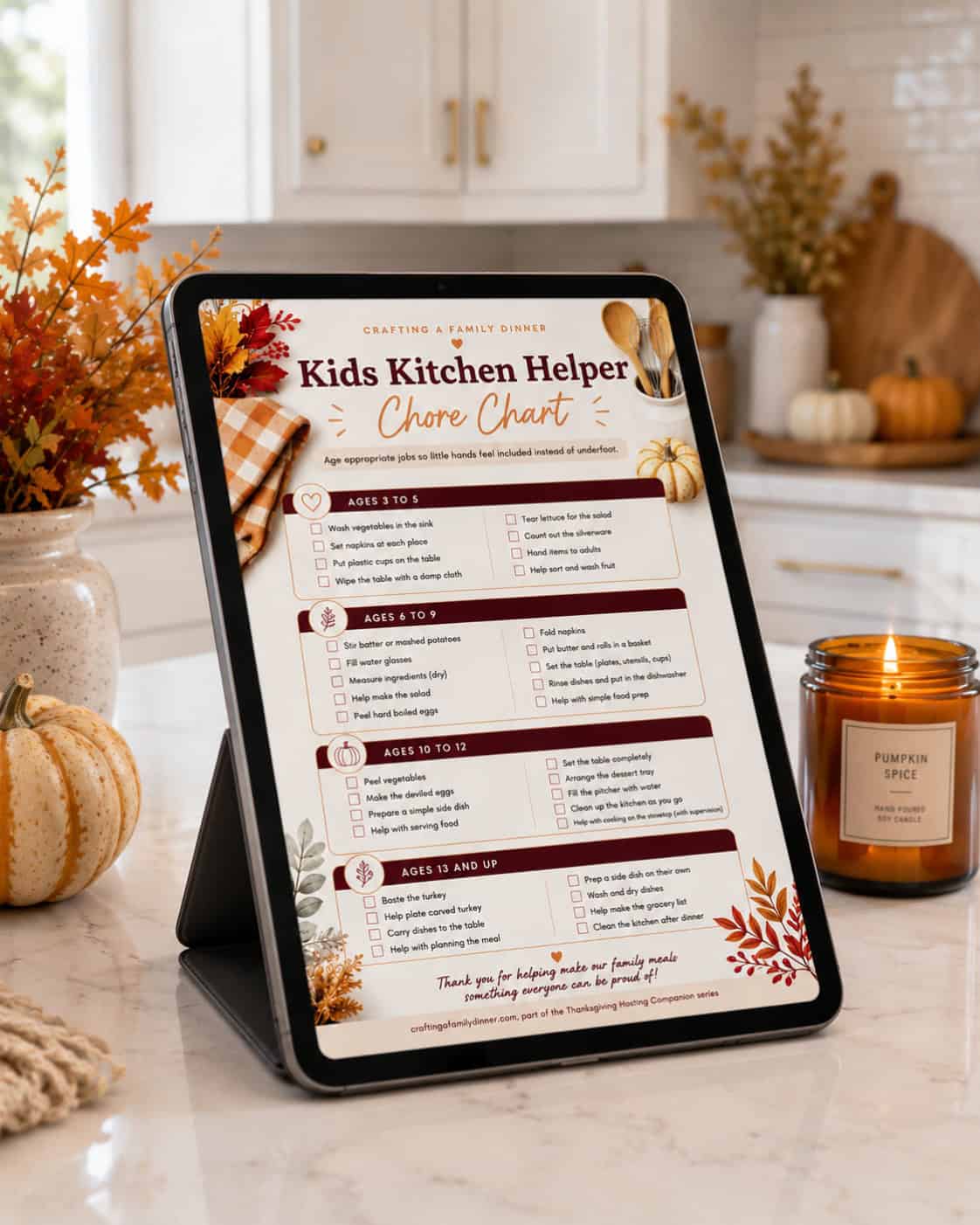 Kids Kitchen Helper Chore Chart printable shown on a tablet in a fall kitchen with small pumpkins, autumn leaves, and a pumpkin spice candle