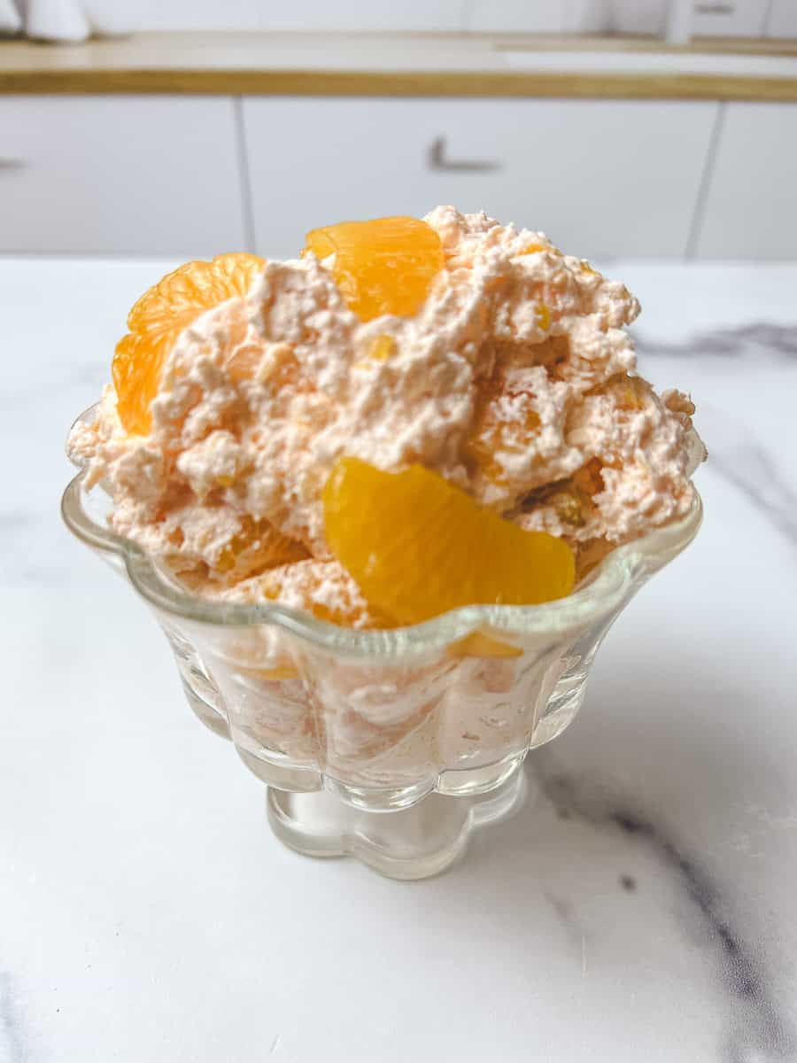 Creamy orange fluff salad mandarin oranges in a footed glass dish, from this orange fluff jello salad recipe