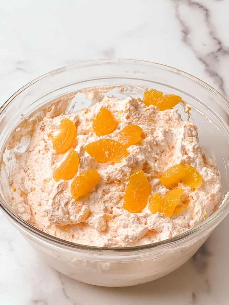 Orange fluff jello salad recipe with mandarin orange fluff mixed in a glass bowl