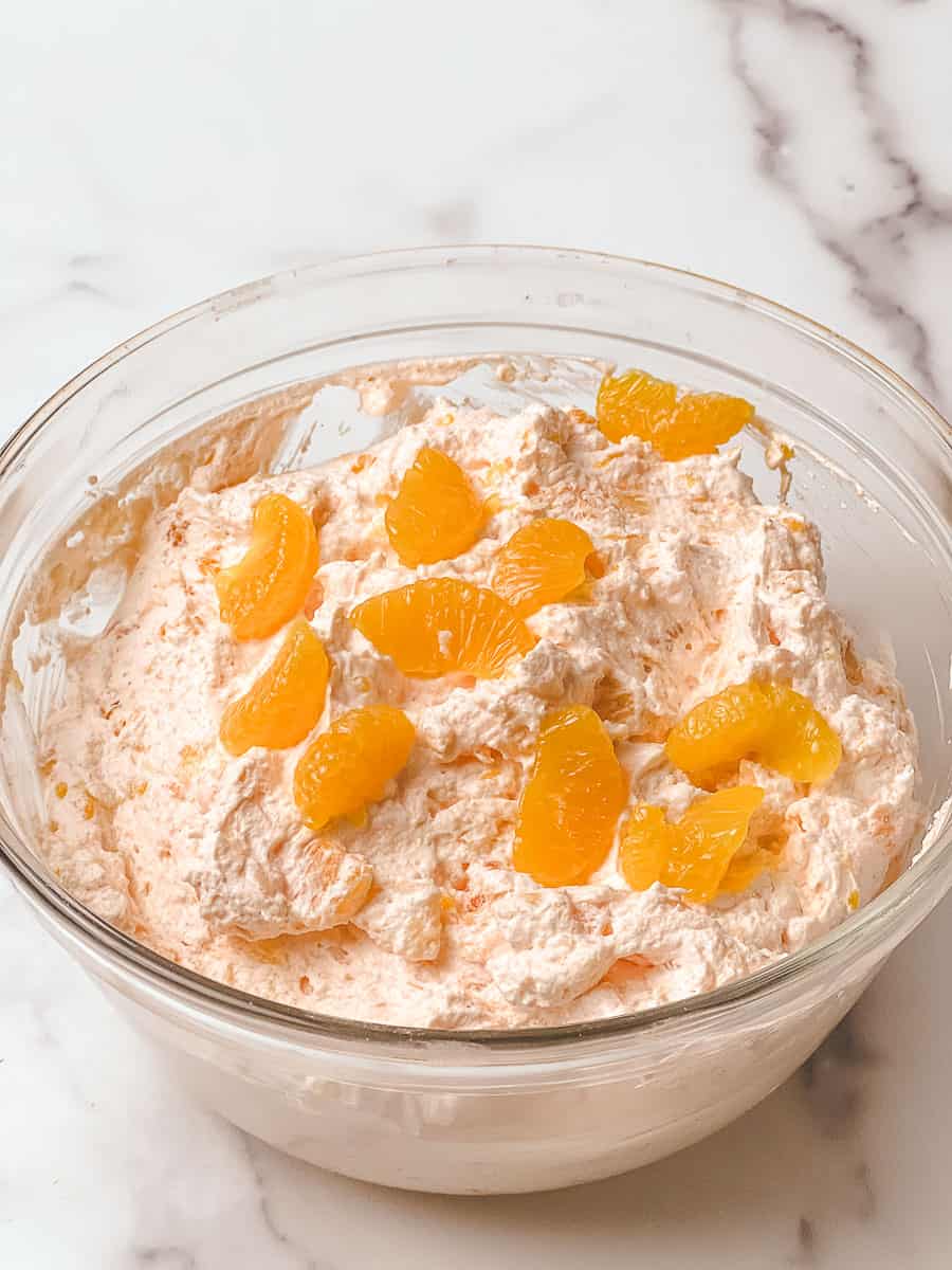 Orange fluff jello salad recipe with mandarin orange fluff mixed in a glass bowl
