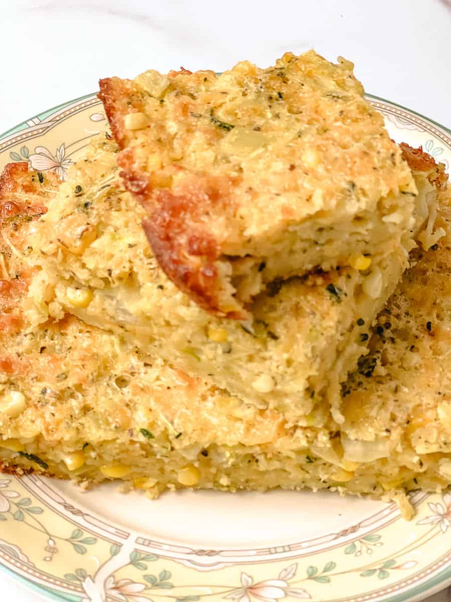 Close up of a zucchini cornbread casserole square showing melted cheddar and whole corn kernels in the tender crumb