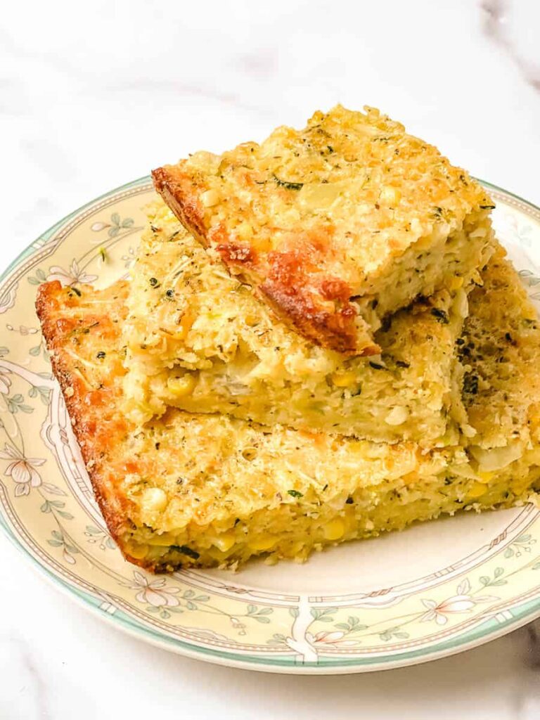 Cheesy zucchini cornbread casserole squares on a vintage floral plate with the browned top crust facing up