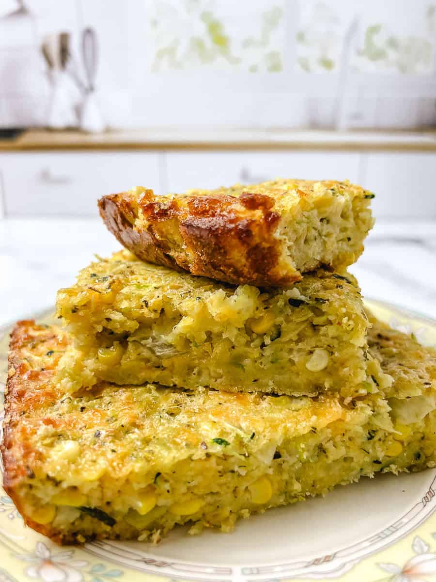 Stacked slices of zucchini cornbread casserole on a floral plate showing sweet corn and shredded zucchini inside the golden crust