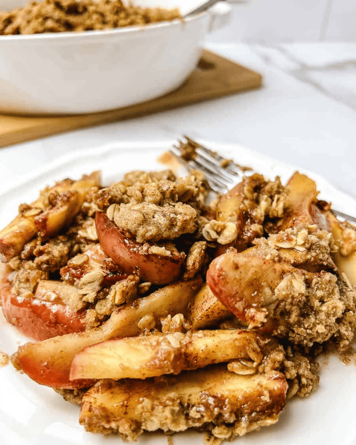 Warm homemade apple crisp with tender baked apples and a golden oat crumble topping, served on a white plate.