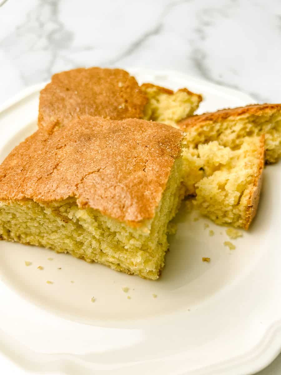 Squares of golden homemade cornbread with a soft, crumbly center on a white scalloped plate, ready to serve with easy crockpot chili.