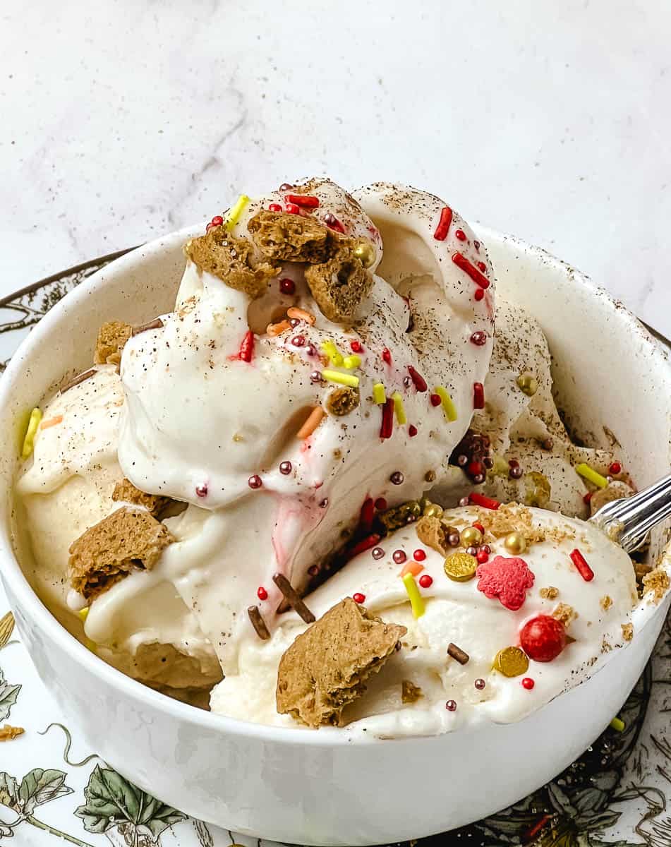 Close up scoop of creamy pumpkin protein ice cream showing the texture, served in a glass bowl with graham cracker topping