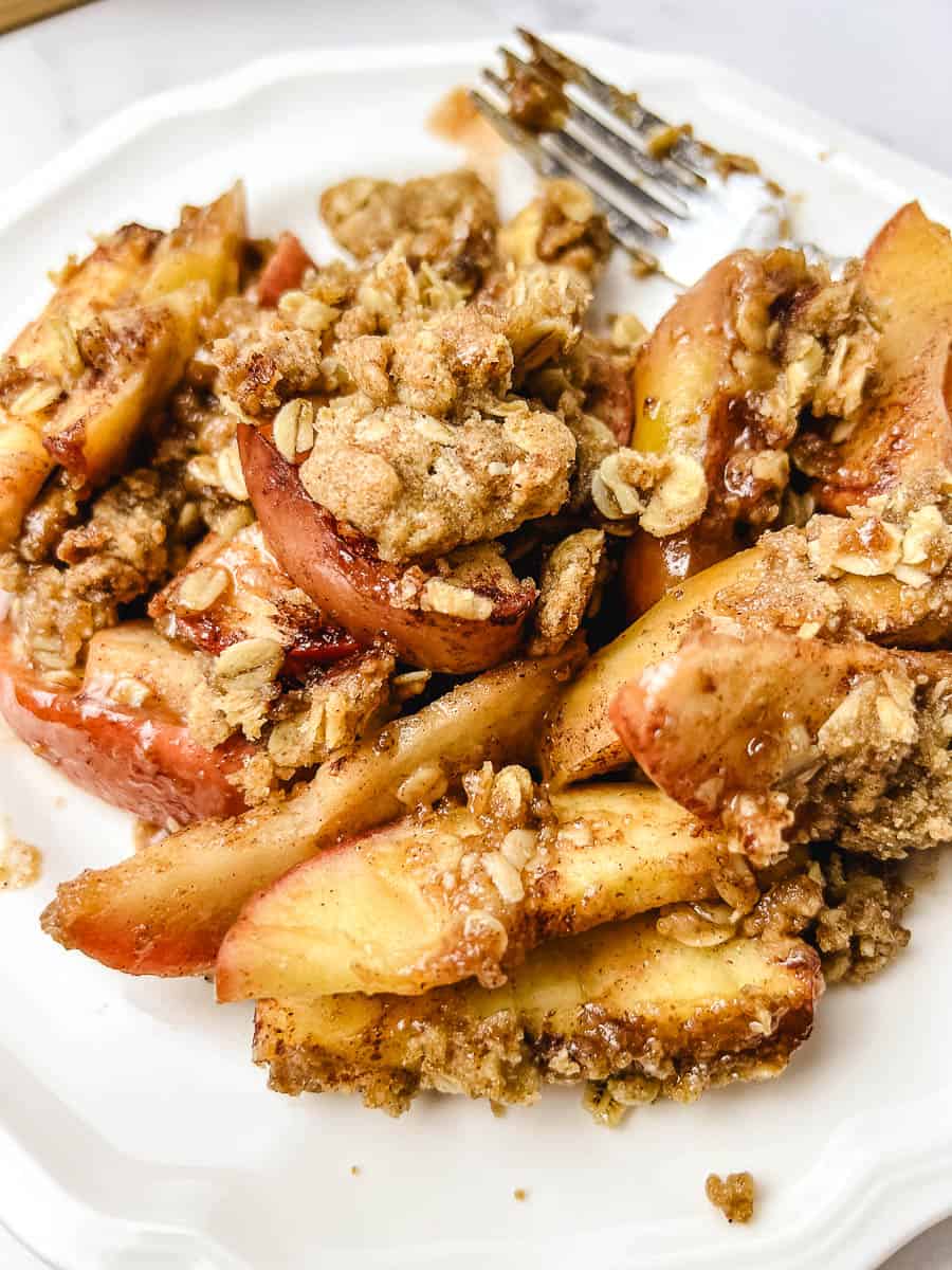 Close-up of warm apple crisp with tender baked apples and a golden oat crumble topping on a white plate.