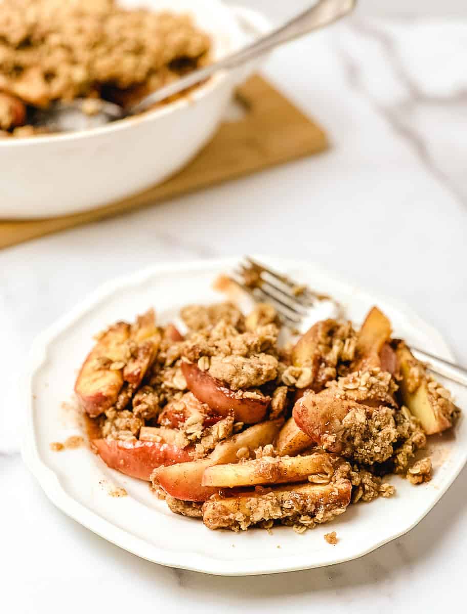 Old-fashioned apple crisp with tender baked apples and a golden oat crumble topping, served on a white plate.