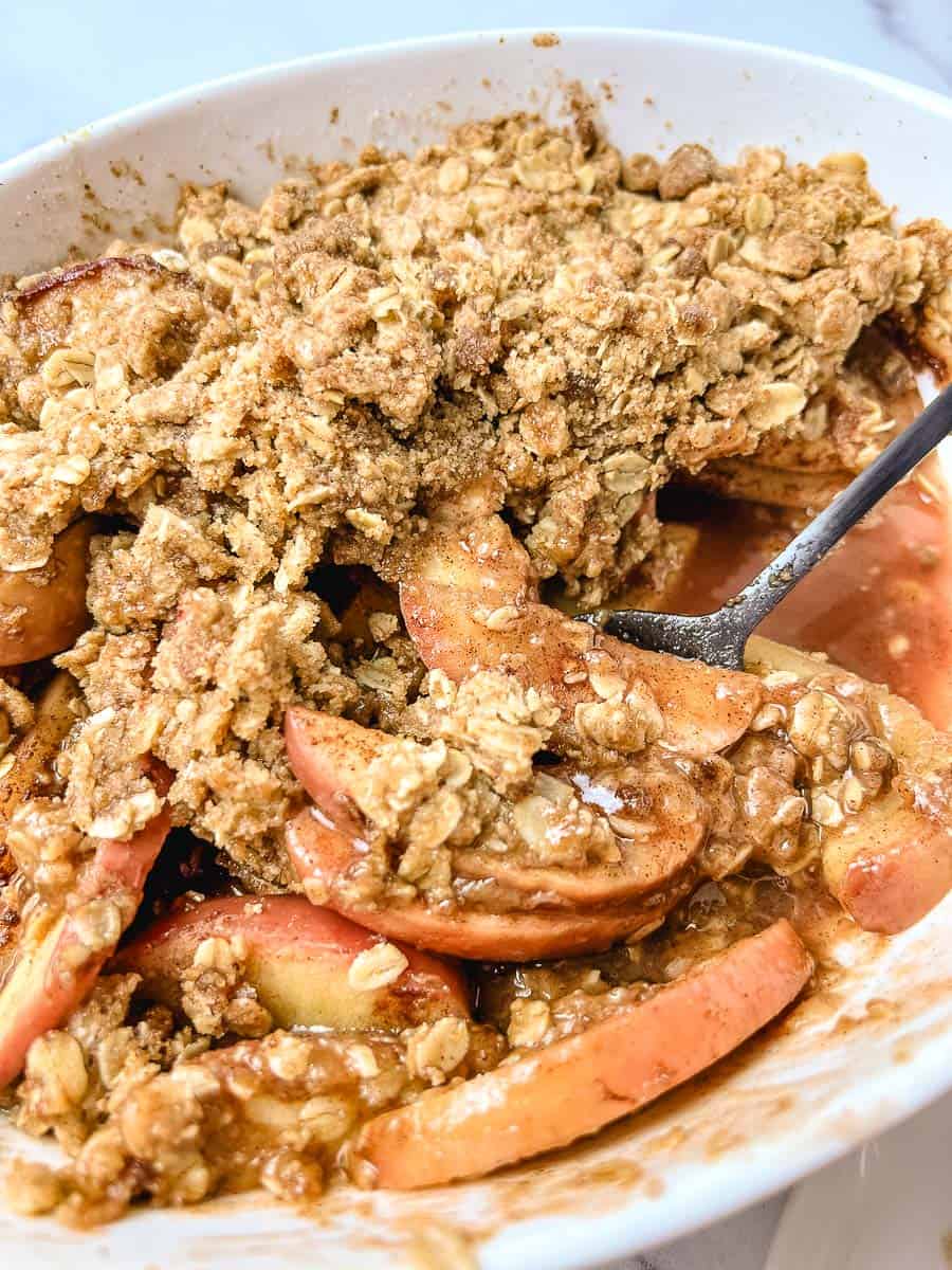 Warm old-fashioned apple crisp with tender cinnamon apples, buttery oat crumble topping, and sweet apple juices in a white baking dish.