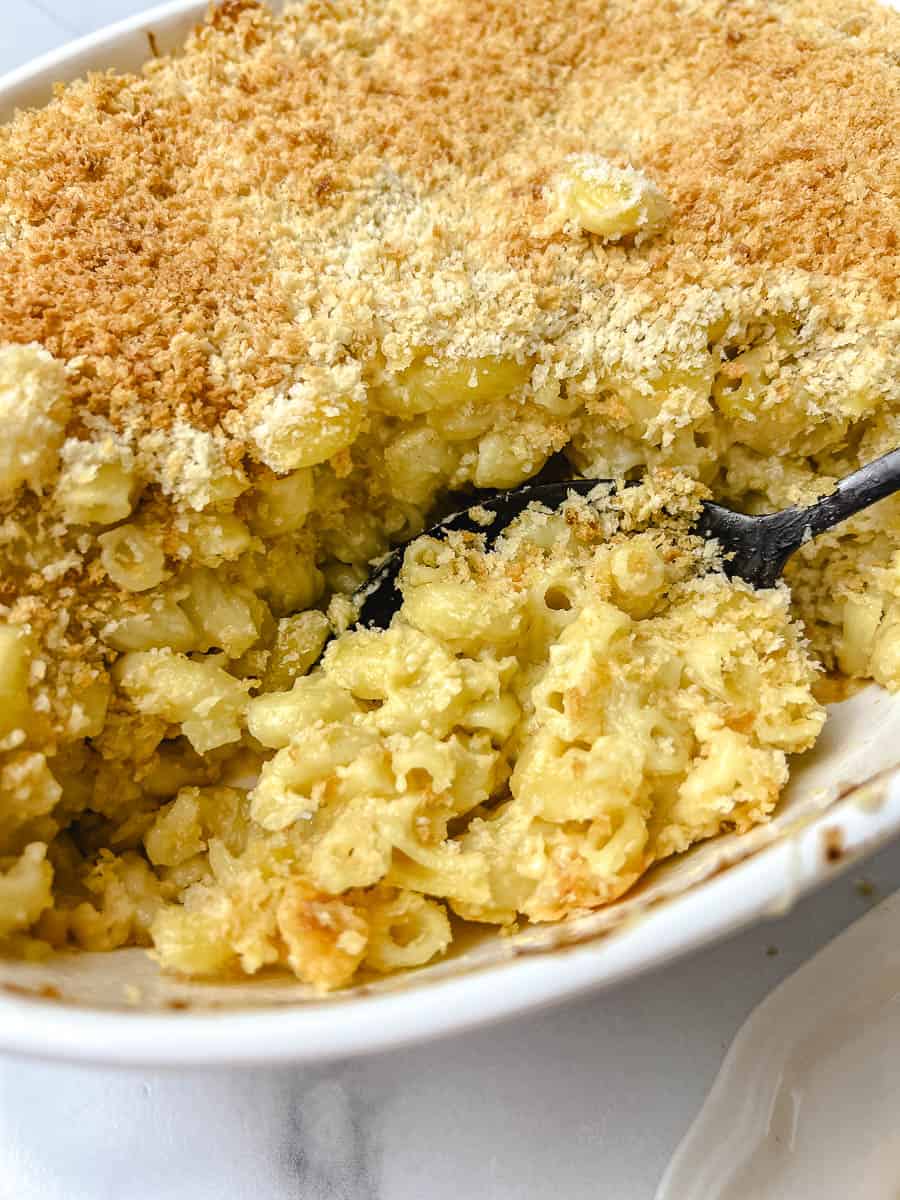 Spoon scooping creamy baked mac and cheese with a crunchy golden panko topping from a white oval casserole dish