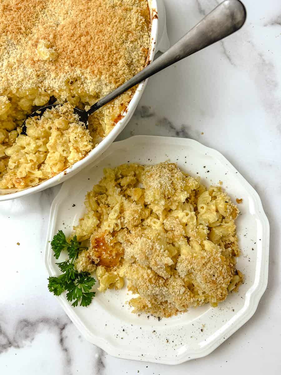 Overhead view of a plate of homemade baked mac and cheese with parsley next to the casserole dish and serving spoon