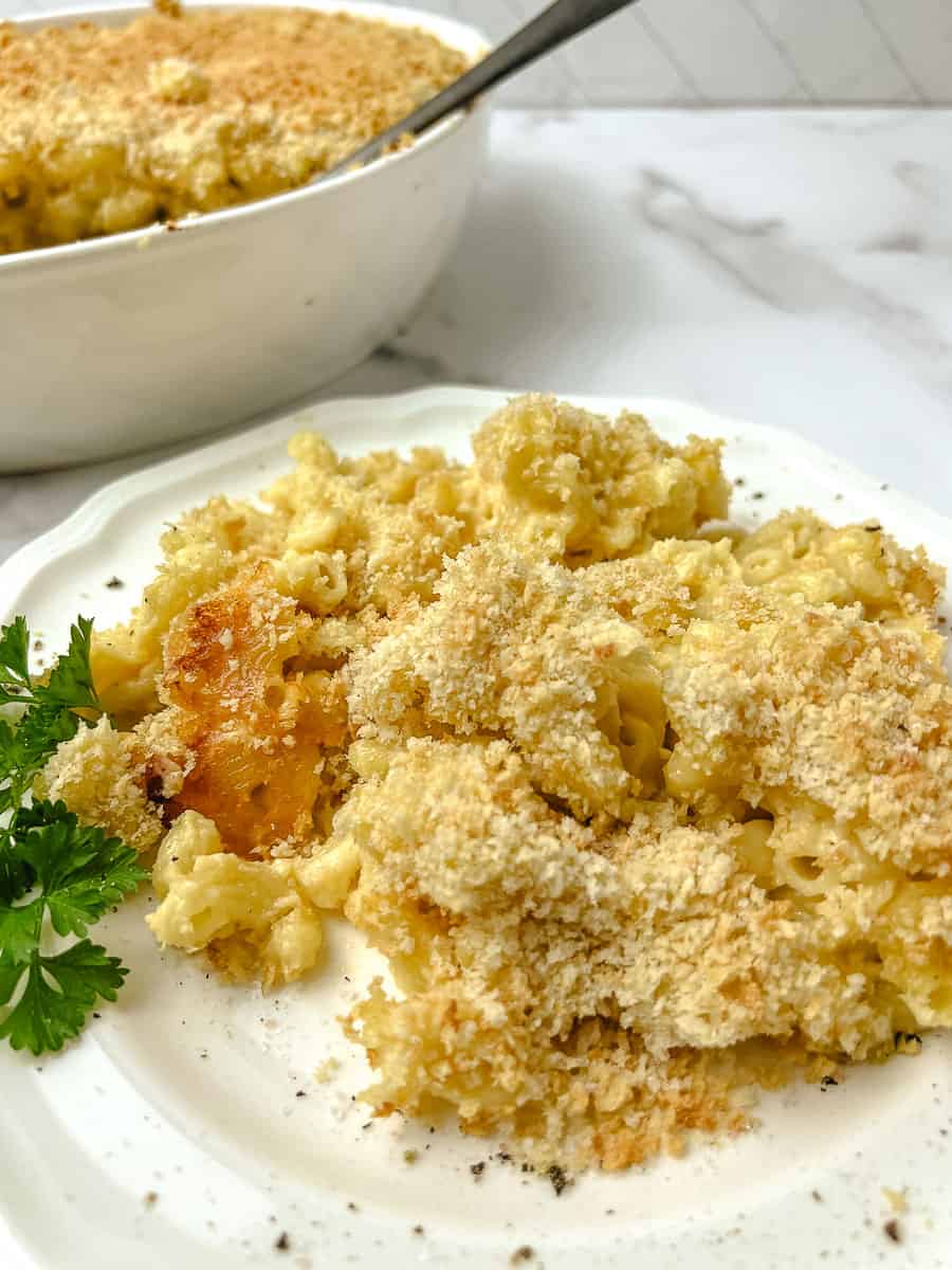 Homemade baked mac and cheese with a crunchy golden panko topping on a white plate, with the oval casserole dish behind it