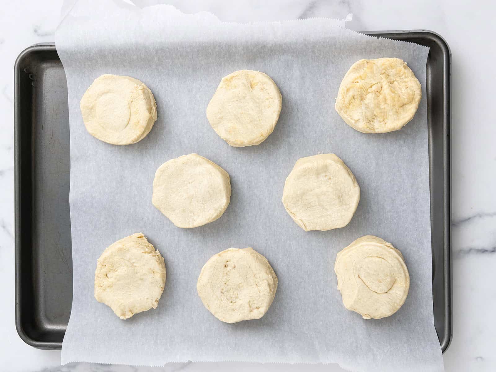 Eight unbaked biscuits for crockpot chicken pot pie on a parchment lined baking sheet, ready for the oven