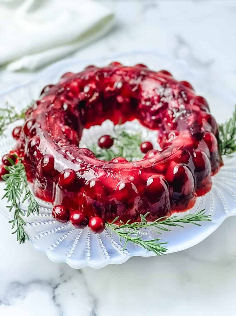 Cranberry jello salad mold turned out on a glass plate, filled with whole cranberries and rosemary sprigs, on a white marble counter