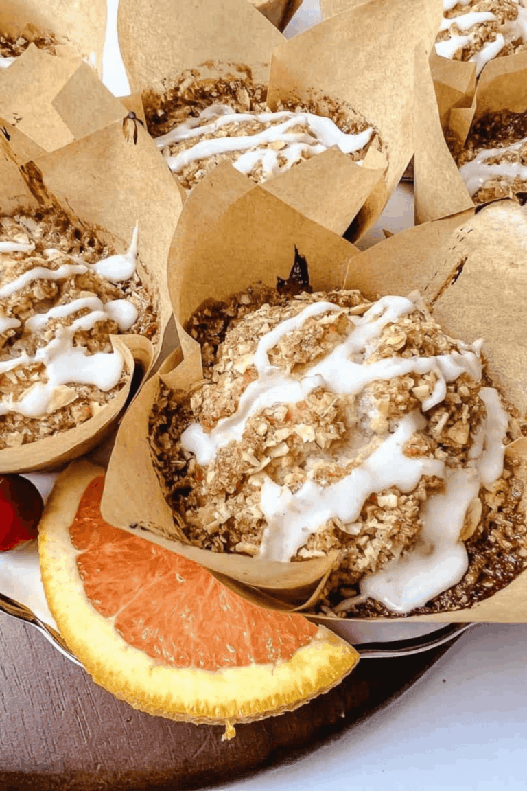 Easy cranberry orange muffins with oat streusel topping and orange glaze in kraft tulip liners, with a fresh orange slice on the plate.