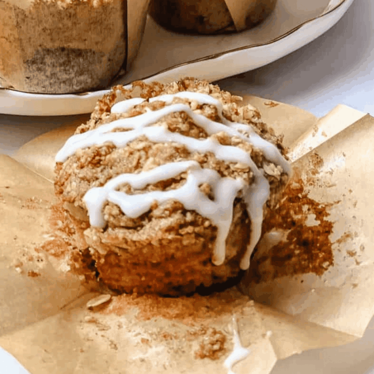 Cranberry orange muffin with oat streusel topping and white glaze drizzle on an unwrapped kraft tulip liner, with more muffins in liners behind it.