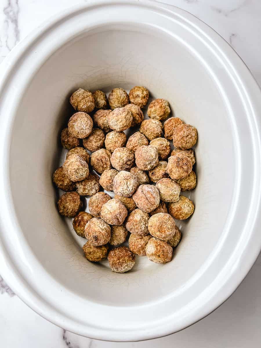 Frozen meatballs in a white crockpot, the first step for making crockpot cranberry meatballs, on a white marble counter