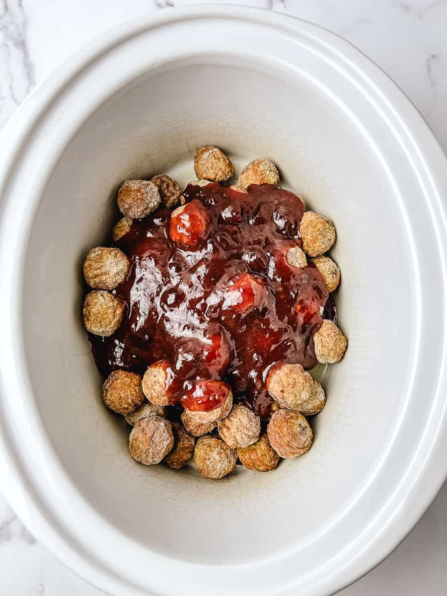 Cranberry chili sauce poured over frozen meatballs in a white crockpot, ready to stir for crockpot cranberry meatballs