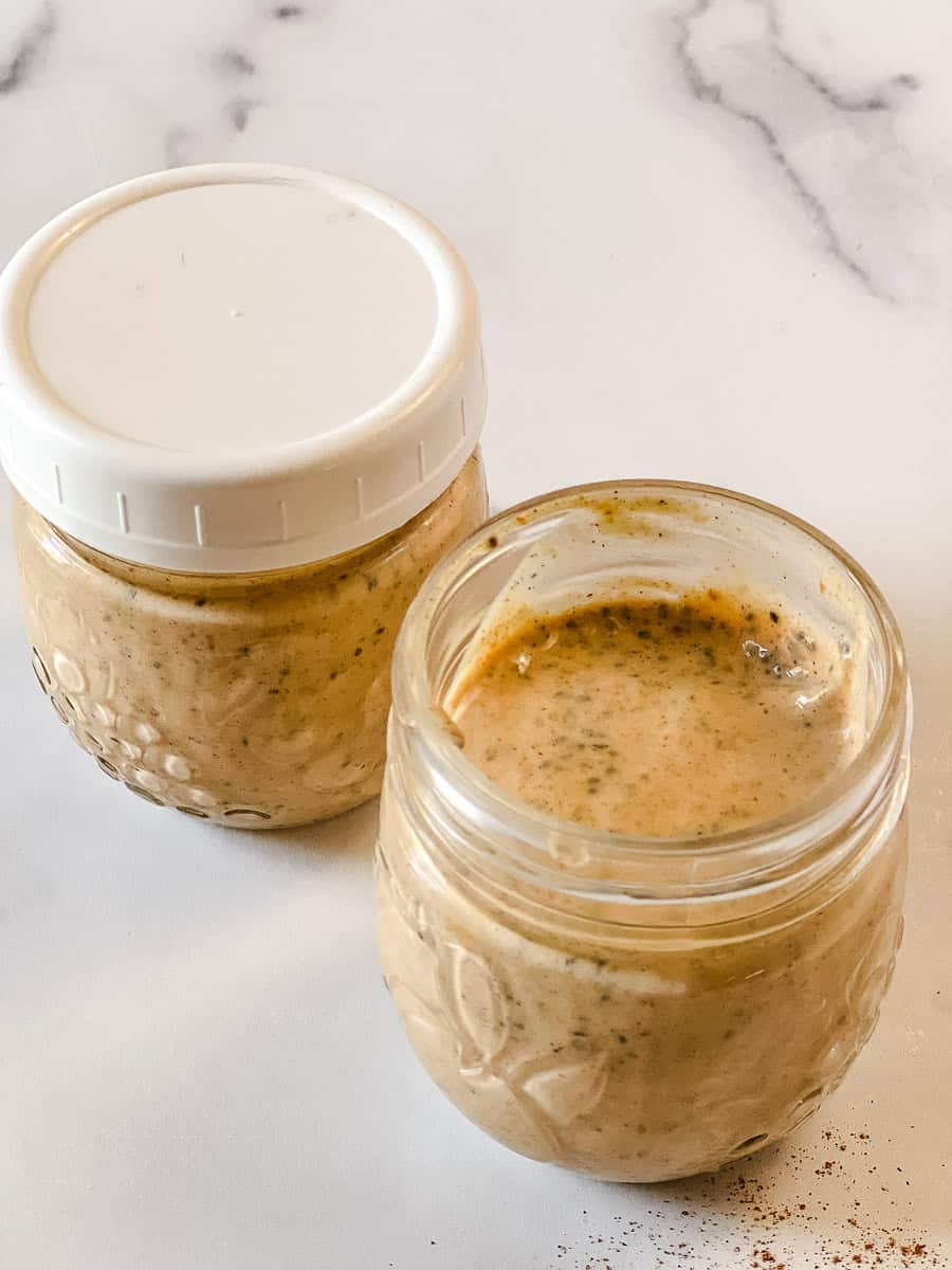 Two glass jars of pumpkin chia seed pudding on a white marble counter, one sealed with a white lid and one open to show the creamy make-ahead breakfast inside.