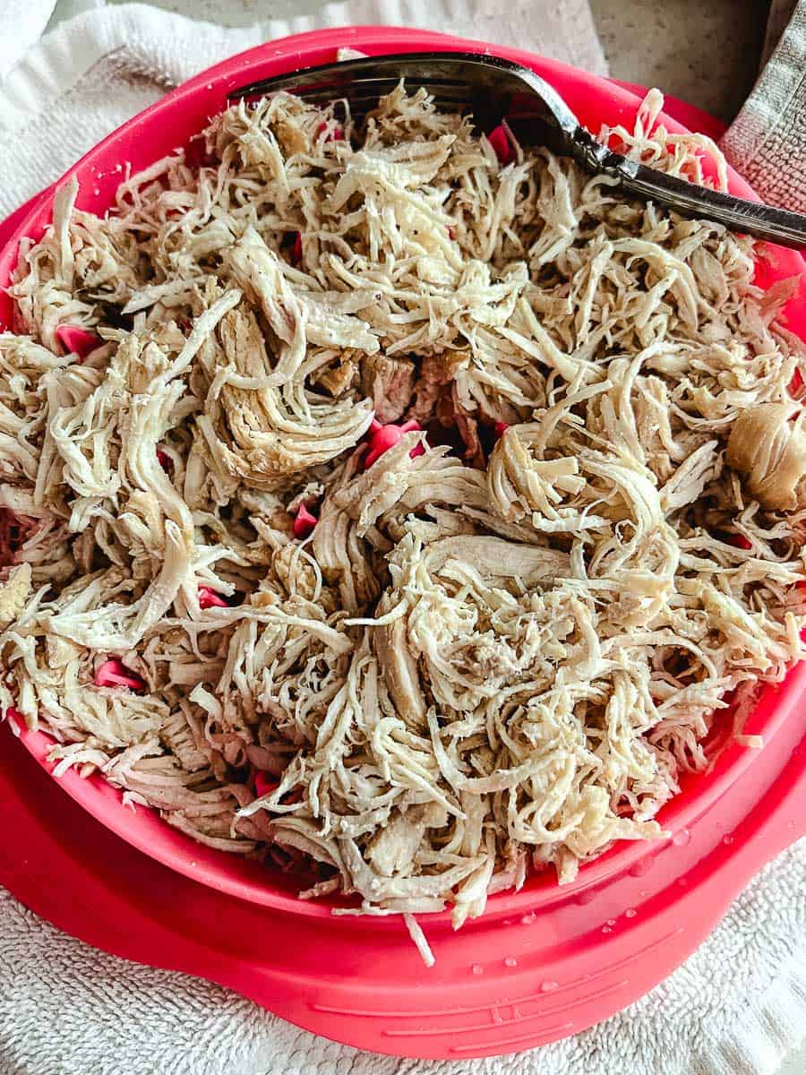 Shredded chicken breast for slow cooker white chicken chili in a bright pink bowl with a fork resting on the edge, set on a white towel